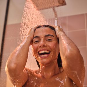 Woman standing in a running shower with pure joy, smiling as she uses the Crometta shower from hansgrohe #AllMyFeels
